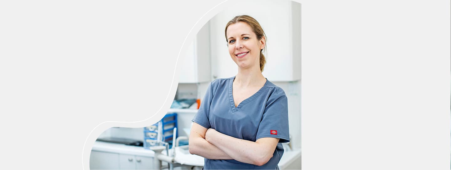 Wellbeing Hero A female dentist in blue scrubs with arms crossed smiling towards the camera
