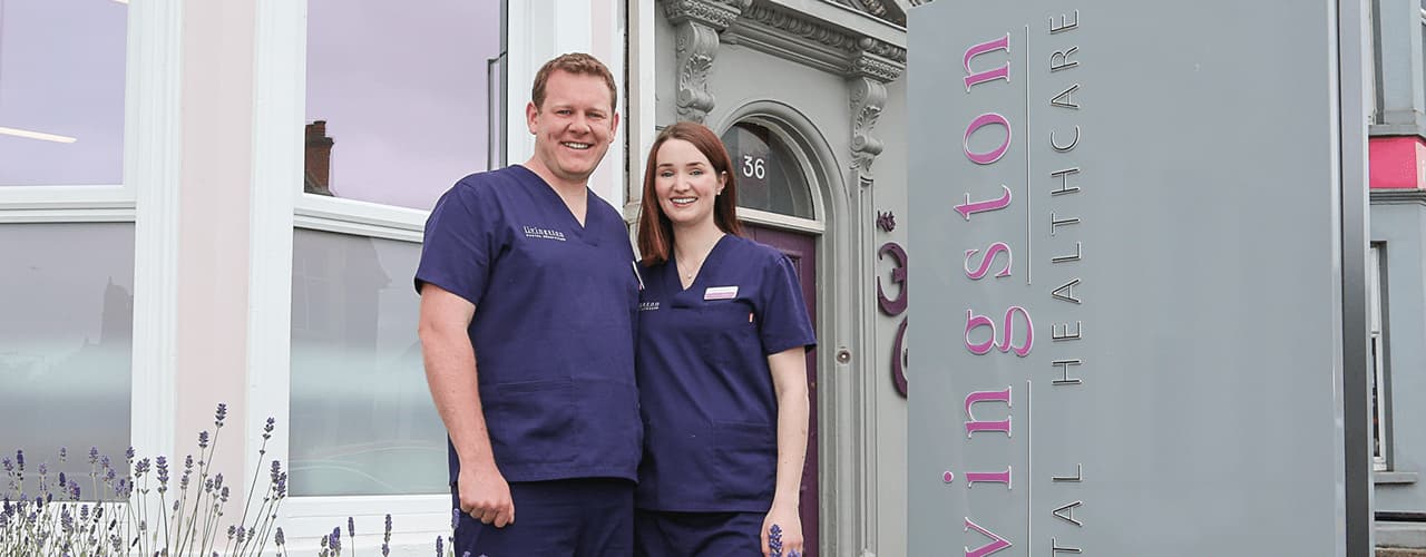 Livingstone Dental Healthcare Ross And Tracey By Sign 1280X500 Ross and Tracey standing by the practice sign outside the practice