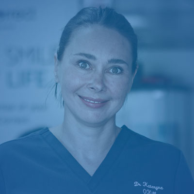 Smiling woman in dental scrubs standing indoors, looking at the camera.