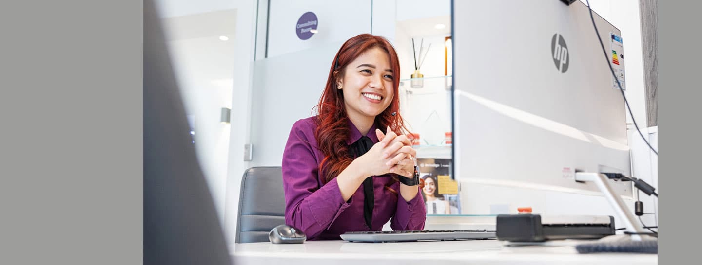 A smiling woman sitting in front of a computer monitor