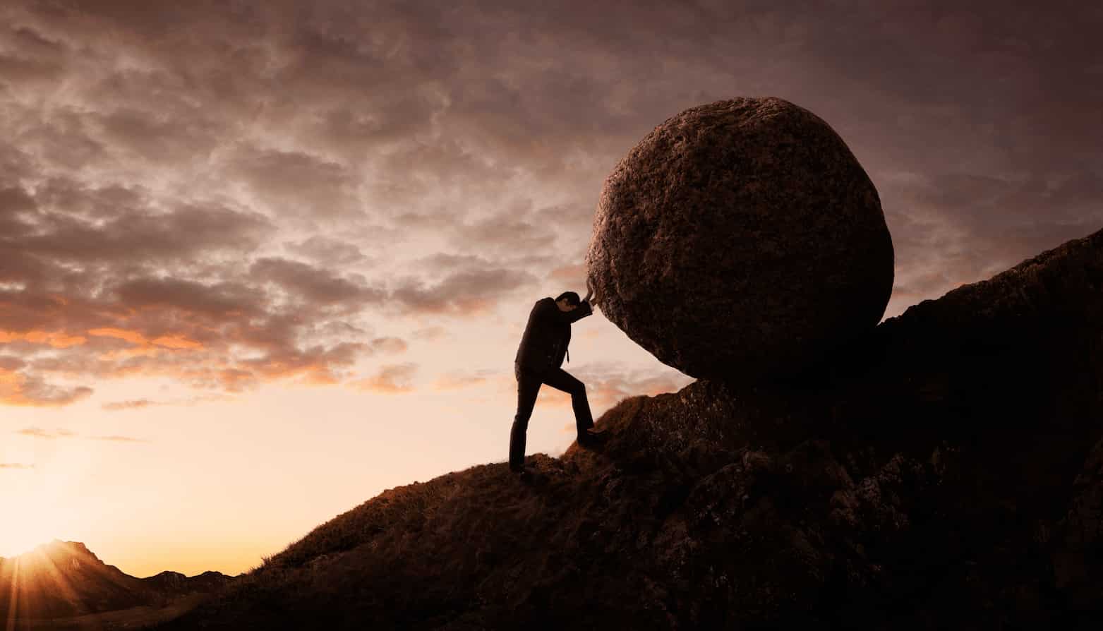 NI Blog Rock A person in silhouette pushes a boulder five times their size up a hill.
