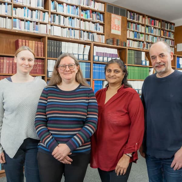 Library Staff featured Amy Grinnell, Helen Nield, Damyanti Raghvani and Peter Folly, standing in front of bookshelves, facing the camera